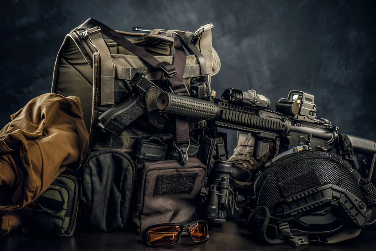 A military backpack alongside a rifle and various tactical gear arranged for outdoor or combat readiness.