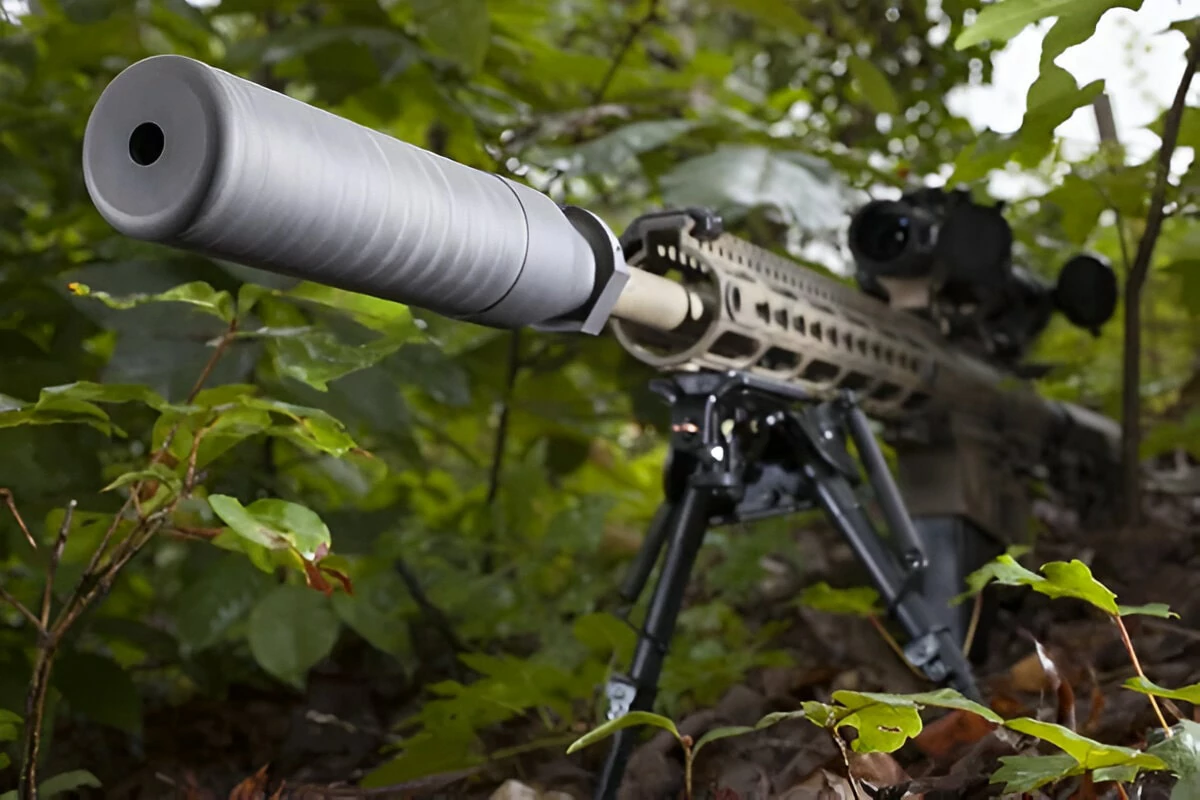 A rifle positioned on a tripod, surrounded by trees in a serene woodland setting.