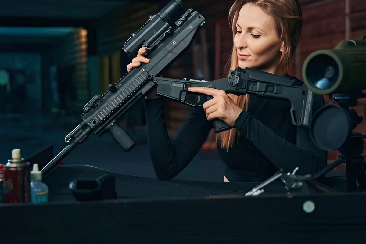 A woman sitting with a rifle, gazing thoughtfully ahead, showcasing strength and focus in her expression.